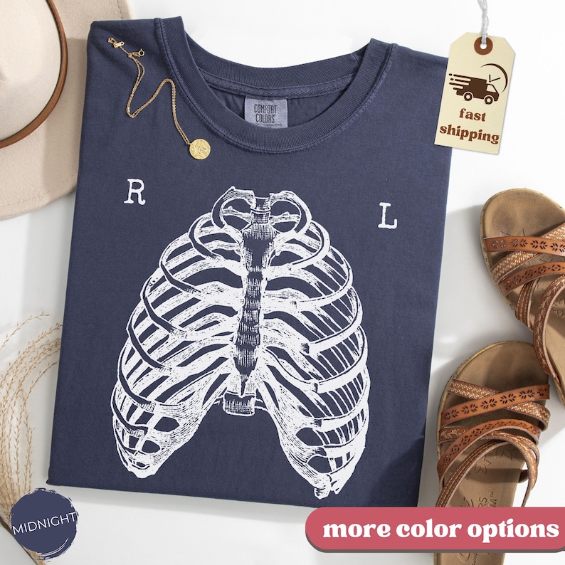 May include: A navy blue t-shirt with a white rib cage graphic. The shirt has the letters "R" and "L" on either side of the rib cage design. A gold necklace and brown sandals are also visible.