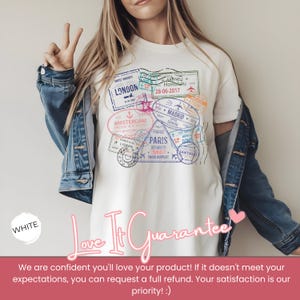 May include: White t-shirt featuring a travel-themed graphic with various city stamps, including London, Paris, and Amsterdam. The design incorporates dates and airport details. The shirt is paired with a denim jacket.