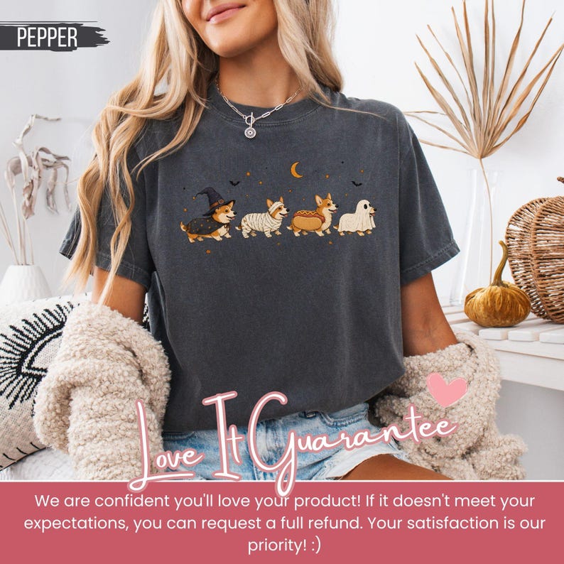 May include: A charcoal grey short-sleeve t-shirt featuring a graphic of four corgi dogs in Halloween costumes, including a witch, a mummy, a hot dog, and a ghost, with a crescent moon and small bats printed above the dogs.