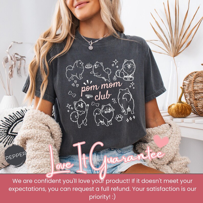 以下が含まれることがあります： ポメラニアン犬の白いグラフィックと「pom mom club」の文字が入った濃い灰色のTシャツ。デザインには犬の骨、星、足跡が含まれています。このTシャツはカジュアルなスタイルです。