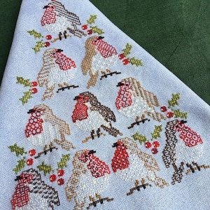 May include: A blue and white cross-stitch design of a Christmas tree with robins and holly berries.