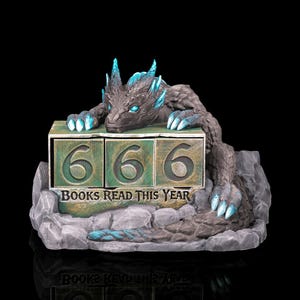 Könnte beinhalten: Graue Drachenfigur mit blauen Akzenten, die auf einem Steinsockel ruht. Der Drache befindet sich vor einem Blockkalender mit der Zahl "666" und dem Text "BOOKS READ THIS YEAR". Die Figur hat ein detailliertes, strukturiertes Aussehen.