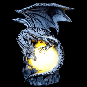 Könnte beinhalten: Silberne Drachenfigur mit ausgebreiteten Flügeln und einem leuchtenden gelben Orb. Der Drache sitzt auf einem felsigen Sockel, mit detaillierten Schuppen und Flügeln. Der Orb strahlt warmes Licht vor schwarzem Hintergrund aus.