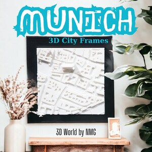 Pode incluir: Um mapa da cidade de Munique, Alemanha, em 3D emoldurado em preto. O mapa é branco e mostra as ruas e os edifícios da cidade. A moldura está em uma parede branca com uma planta no fundo. O texto "3D City Frames" e "3D World by NMG" é visível abaixo da moldura.