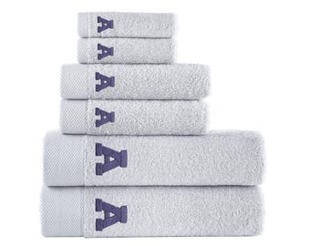 May include: A stack of six light gray bath towels with the letter "A" embroidered in a darker blue color. The towels are arranged in a pyramid shape, with the largest towel at the bottom and the smallest at the top. The towels are made of a soft, absorbent material.