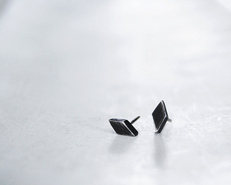 May include: A pair of small, black diamond-shaped earrings. The earrings are made of metal and have a simple, minimalist design.