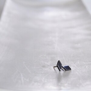 May include: A pair of small, black, diamond-shaped earrings on a white surface.