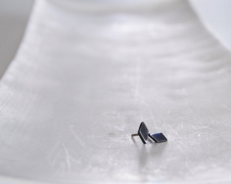 May include: A pair of small, black, diamond-shaped earrings on a white surface.