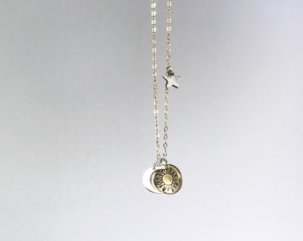 May include: A silver chain necklace with a star charm and a sun and moon charm. The sun charm is gold and has a detailed design.