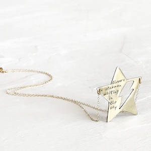 May include: A gold-toned necklace with a star-shaped pendant. The pendant has a cut-out design and the words "There's a starman waiting in the sky" inscribed on it.