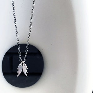 May include: A silver chain necklace with a pair of small, silver wings as a pendant.