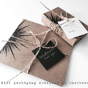 K&ouml;nnte beinhalten: Eine braune Geschenkbox aus Papier mit einem schwarzen Etikett, auf dem "handgefertigt f&uuml;r dich" steht. Die Box ist mit Schnur gebunden und hat ein Sternburst-Design. Die Box steht auf einer wei&szlig;en Oberfl&auml;che.