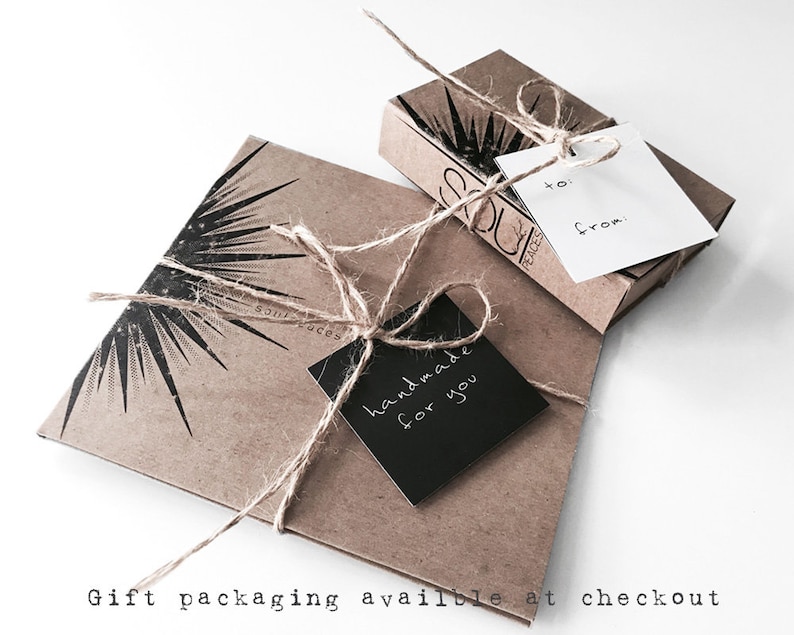 K&ouml;nnte beinhalten: Eine braune Geschenkbox aus Papier mit einem schwarzen Etikett, auf dem "handgefertigt f&uuml;r dich" steht. Die Box ist mit Schnur gebunden und hat ein Sternburst-Design. Die Box steht auf einer wei&szlig;en Oberfl&auml;che.