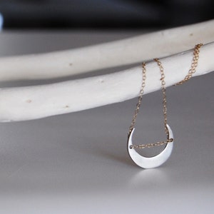 Op de afbeelding: Een zilveren halve maan hanger ketting met een delicate gouden ketting.