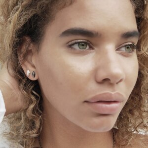 May include: A close-up of a person's face with a focus on their eyes and lips. They are wearing small, geometric earrings in both ears.