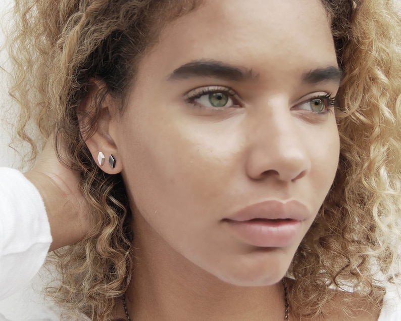 May include: A close-up of a person's face with a focus on their eyes and lips. They are wearing small, geometric earrings in both ears.