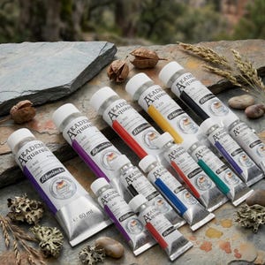 Könnte beinhalten: Eine Auswahl an Schmincke Akademie Aquarell Aquarellfarben-Tuben in verschiedenen Farben. Die silbernen Tuben haben weiße Kappen und farbcodierte Streifen. Die größte Tube ist 60 ml, die kleineren sind 15 ml.