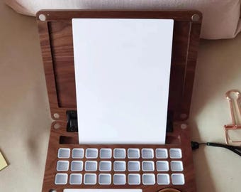May include: A wooden artist's palette with a hinged lid, featuring a white paper surface, a grid of small paint wells, a large mixing area, and a brass-colored circular well. The palette is open, ready for use.