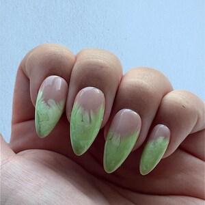 May include: Close-up of five almond-shaped nails with a light green and white marbled design. The nails are painted with a light pink base and have a light green marbled design on the tips.