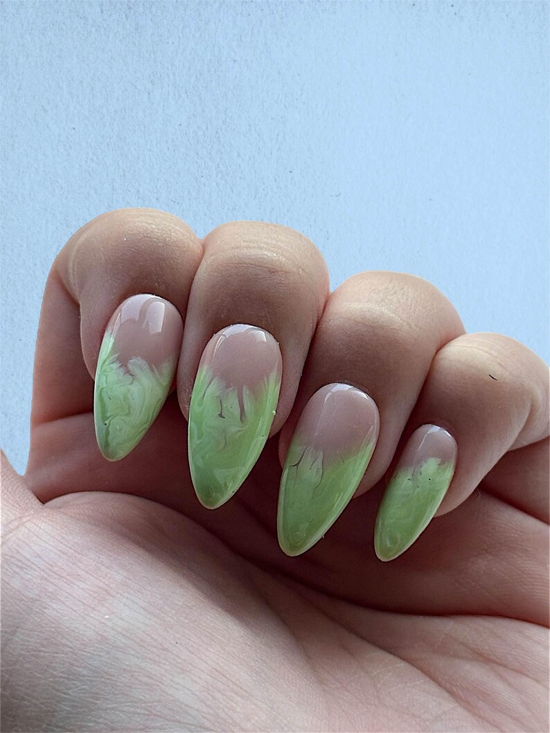 May include: Close-up of five almond-shaped nails with a light green and white marbled design. The nails are painted with a light pink base and have a light green marbled design on the tips.