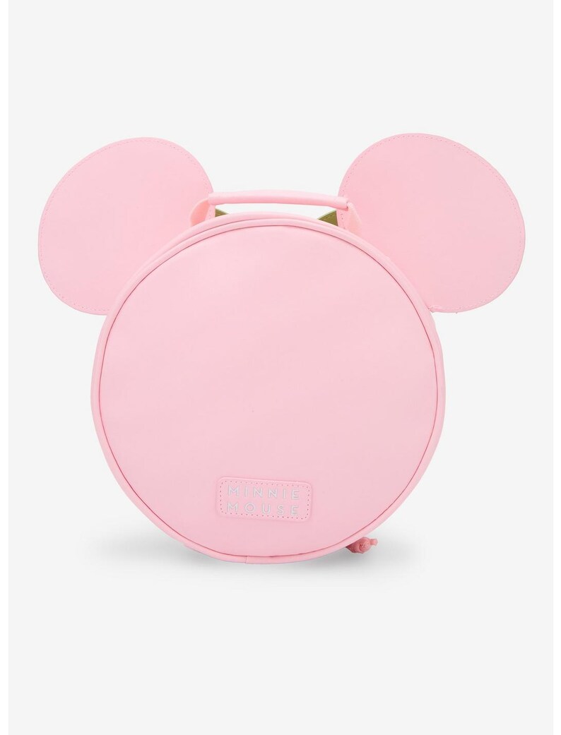 May include: A light pink, round handbag with two large, rounded ears on top, resembling a mouse. The bag has a handle and the text "MINNIE MOUSE" is visible on the front.