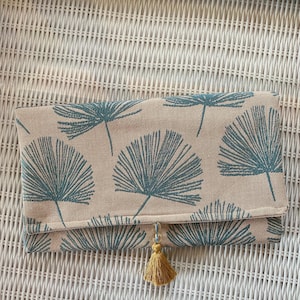 Cartera de mano en turquesa y beige con estampado de hojas tropicales. Esta cartera es reversible. Forro de terciopelo tostado y adorno de borlas y cuentas doradas.