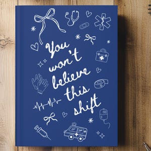 Op de afbeelding: Een marineblauw notitieboek met witte illustraties van medische symbolen en de tekst "You won't believe this shift." Het notitieboek is omringd door pennen, een laptop en een kleine plant op een houten oppervlak.