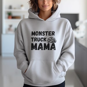 May include: A light gray hoodie with a front pocket and a drawstring hood. The front of the hoodie features the text "MONSTER TRUCK MAMA" in black block letters, with a monster truck graphic above the word "MAMA".