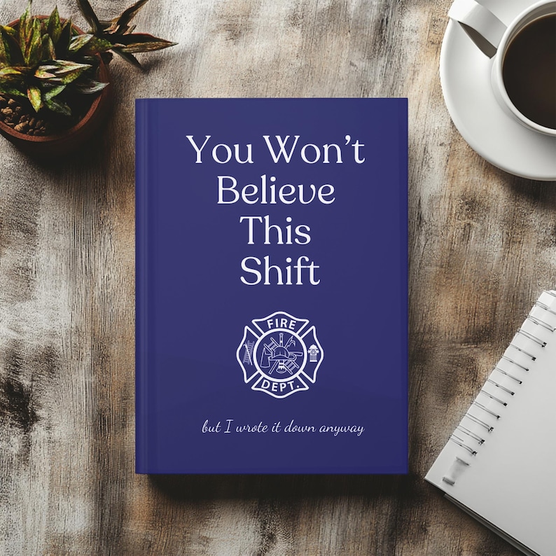 May include: A navy blue journal with the text "You Won't Believe This Shift" and a fire department emblem. The phrase "but I wrote it down anyway" is printed at the bottom. A cup of coffee and a small plant are in the background.