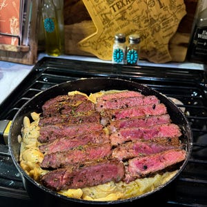 Puede incluir: Una sart&eacute;n con filete en rodajas cocinado con una salsa cremosa. El filete est&aacute; sazonado y tiene un interior rosado. Una tabla de cortar de madera con forma de Texas y saleros y pimenteros est&aacute;n en el fondo.