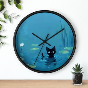 May include: A round wall clock with a black frame. The clock face features a whimsical illustration of a black cat in a pond with lily pads. The cat has blue eyes and is surrounded by water. The clock hands are black.