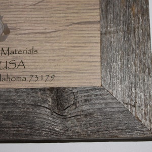 May include: Close-up of a wooden picture frame with a light brown background and a dark gray wood frame. The background has the text "Recycled Materials in the USA, Oklahoma 73179" printed on it.