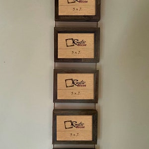 May include: Five rustic wood picture frames hanging vertically on a wall. Each frame has a brown wood finish and a clear glass front. The frames are all the same size and have a small label in the bottom right corner that says "Rustic decor 5x7".