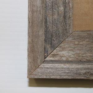 Pu&ograve; includere: Primo piano di un angolo di una cornice per foto in legno rustico. La cornice &egrave; realizzata in legno riciclato con una finitura grigia naturale.