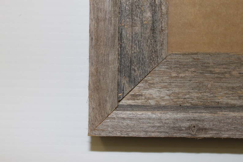 Pu&ograve; includere: Primo piano di un angolo di una cornice per foto in legno rustico. La cornice &egrave; realizzata in legno riciclato con una finitura grigia naturale.