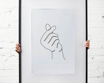Op de afbeelding: Een zwart ingelijst afdruk van een enkele lijntekening van een hand die een hartvorm maakt.