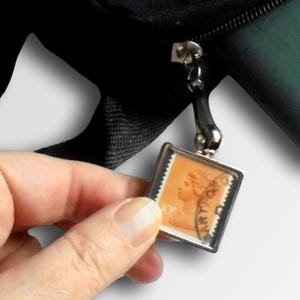 May include: A small, framed, vintage postage stamp with a floral design. It can be used as a keychain, zipper pull, or handbag charm.  TangleCrafts.co.uk