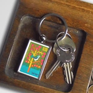 May include: A wooden tray with a key holder, two keys, and a small coin tray with several coins. The key holder has a metal keychain with a colorful bird on a tree design. The text "0.35" is visible on the keychain.