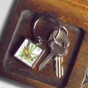 May include: A wooden tray with two compartments. One compartment holds keys and a keychain with a small square image. The other compartment contains several coins. The tray is made of dark wood.
