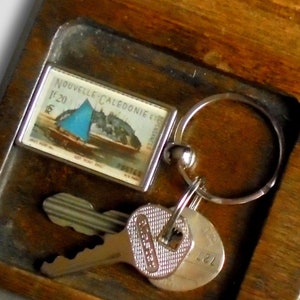 May include: A wooden tray with compartments for keys, coins, and other small items. The tray has a dark brown stain and is made of wood. The tray has a compartment for keys, a compartment for coins, and a compartment for other small items. The tray is empty except for a key ring with a small stamp attached to it.