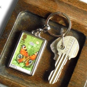 May include: A wooden key holder with a separate compartment for change. The key holder has a key ring with a butterfly charm and a key. The change compartment has several coins.