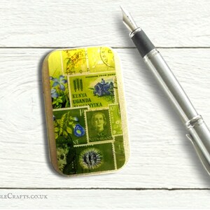 May include: A small, rectangular tin with a collage of vintage postage stamps featuring images of flowers, a tractor, a woman's portrait, and text in various languages, including "Kenya", "Uganda", and "Nederland".