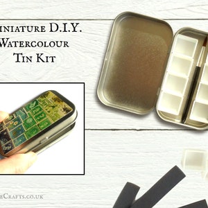 May include: A miniature tin kit for watercolour painting. The kit includes a metal tin with a colourful design, 8 paint pans, and a small brush. The tin is open and the paint pans are visible. The kit is on a white wooden surface.