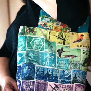May include: A tote bag made from fabric with a collage of colourful postage stamps from around the world. The stamps feature images of animals, people, and landmarks. The bag has a black strap.