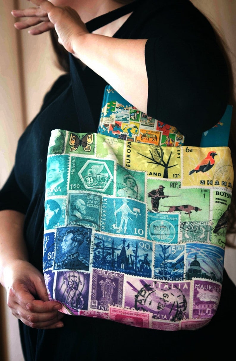 May include: A tote bag made from fabric with a collage of colourful postage stamps from around the world. The stamps feature images of animals, people, and landmarks. The bag has a black strap.