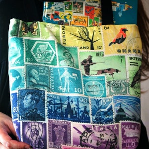 May include: A colourful tote bag with a patchwork design featuring vintage postage stamps from around the world. The bag has a green, blue, and white background with images of birds, trees, and ships. The text on the stamps includes "Ghana", "Botswana", "Helvetia", "Rep. E", "Europa", "United States Postage", "Italia", "Mauritius", "Service Postage", "India", and "United States Postage".