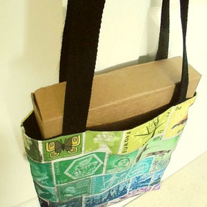 May include: A colourful tote bag made from fabric with a patchwork design of vintage postage stamps. The bag has black straps and is holding a brown cardboard box.