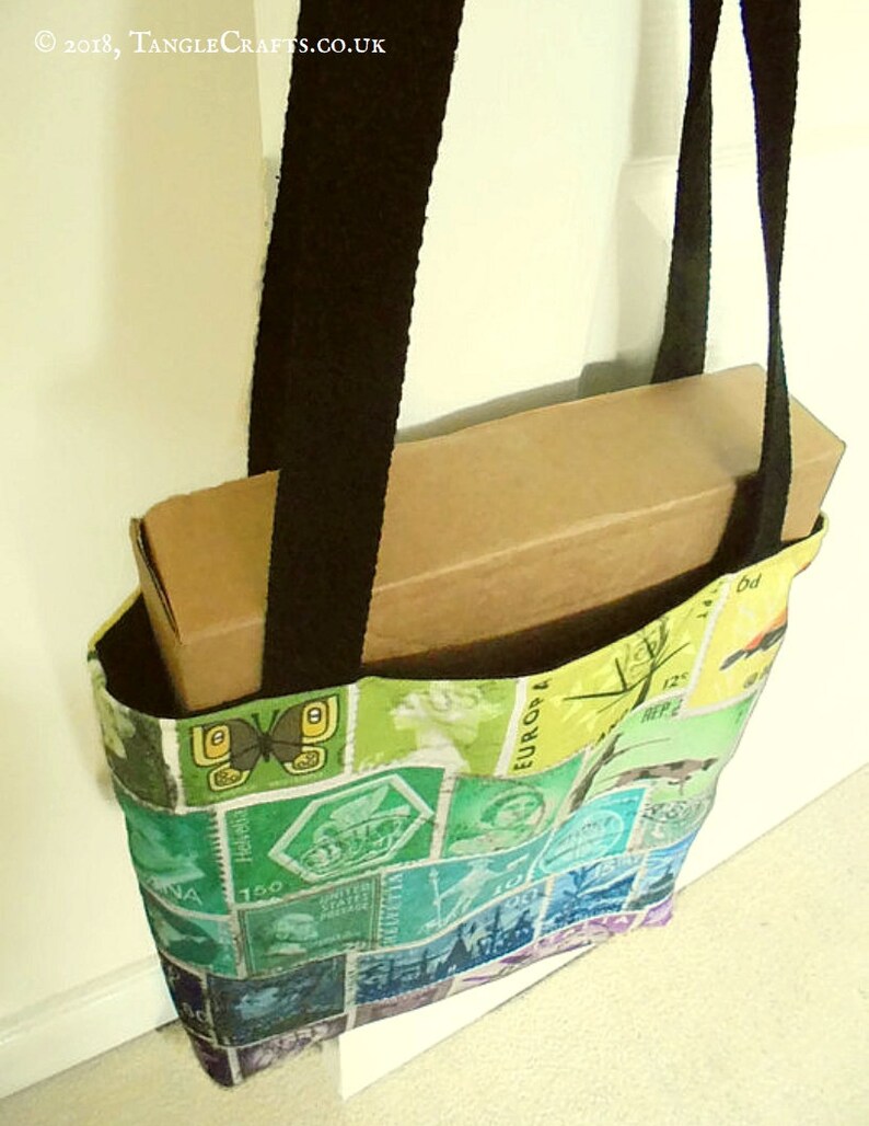 May include: A colourful tote bag made from fabric with a patchwork design of vintage postage stamps. The bag has black straps and is holding a brown cardboard box.