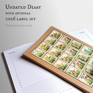 May include: An undated diary with a 2026 label set. The diary is open to the October page, with a grid for notes. A rectangular box of vintage stamps with floral and bird illustrations rests on top.