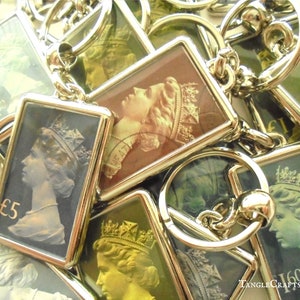 May include: A group of silver keychains with a rectangular image of a queen's profile on a stamp. The stamps feature different denominations, including "£5" and "£1.60".